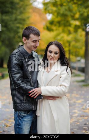 Un homme embrasse sa femme enceinte. Un homme dans une veste noire embrasse et embrasse une femme dans un manteau blanc. Automne Banque D'Images