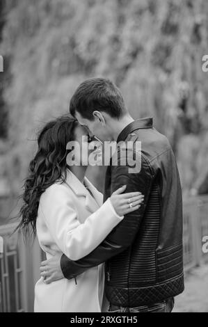 Un homme embrasse sa femme enceinte. Un homme dans une veste noire embrasse et embrasse une femme dans un manteau blanc. Automne Banque D'Images