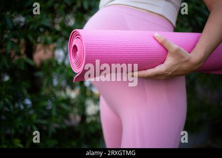 une jeune femme enceinte tient un tapis de yoga rose dans ses mains. gros plan Banque D'Images