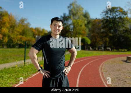 Portrait d'un athlète asiatique souriant et confiant debout devant la caméra dans un stade avec ses bras sur les côtés. Banque D'Images