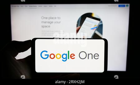 Personne tenant le téléphone portable avec le logo du service d'abonnement de logiciel Google One sur l'écran en face de la page Web d'affaires. Concentrez-vous sur l'affichage du téléphone. Banque D'Images