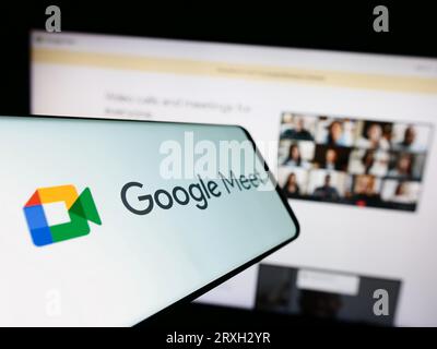Téléphone mobile avec logo du service de communication vidéo Google Meet sur l'écran en face du site Web de l'entreprise. Concentrez-vous sur le centre gauche de l'écran du téléphone. Banque D'Images