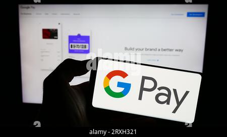 Personne tenant le téléphone portable avec le logo du service de paiement mobile Google Pay sur l'écran en face de la page Web d'affaires. Concentrez-vous sur l'affichage du téléphone. Banque D'Images