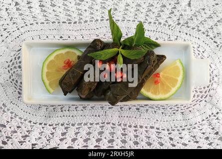 Un plateau de dolma garni de citron, de promegranate et de menthe sur fond de crochet. Banque D'Images