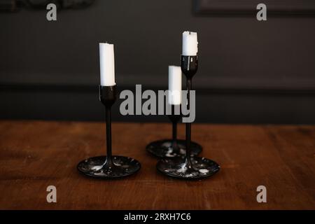 Moderne trois chandeliers en verre noir avec des bougies blanches sur une table en bois de style antique sur fond de mur sombre. Décoration minimaliste et élégante avec chandelles Banque D'Images