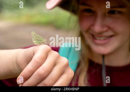 Gros plan d'une jeune fille regardant la papillons de nuit (lépidoptère) qui a atterri sur sa main ; Yukon, Canada Banque D'Images