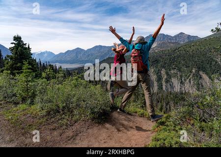 Deux personnes sur une montagne sautant les mains levées et ayant un bon moment lors d'une randonnée dans la nature sauvage du Yukon ; Yukon, Canada Banque D'Images