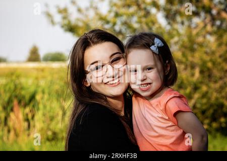 Portrait d'une sœur aînée passant du temps de qualité avec sa petite sœur dans un parc municipal au cours d'une chaude après-midi d'automne ; Leduc, Alberta, Canada Banque D'Images