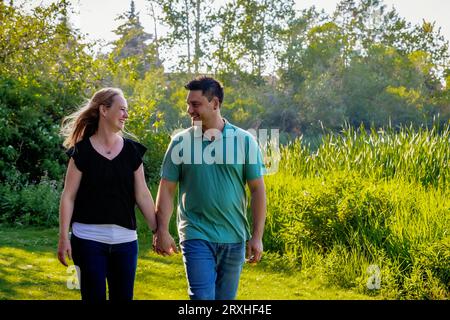 Mari et femme marchant et se tenant la main tout en passant du temps de qualité ensemble dans un parc municipal pendant un après-midi chaud d'automne ; Leduc, Alberta, Canada Banque D'Images