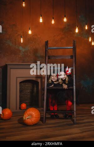 Des petites sorcières se tiennent appuyées sur les escaliers, souriantes. Il y a des citrouilles à proximité et des lanternes brûlent en arrière-plan. Halloween. Banque D'Images