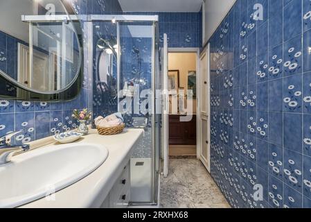 salle de bains avec meuble en bois avec lavabo en porcelaine blanche, cabine de douche et carrelage bleu vintage sur les murs Banque D'Images