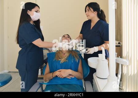 Dentiste femelle avec l'aide de son assistant fixant les dents d'une patiente femme dans la chaise de dentistes. Dentiste examinant les dents d'un patient et ayant un dentaire Banque D'Images