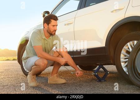 Homme changeant la roue de la voiture sur le bord de la route Banque D'Images