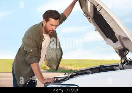 Homme bouleversé regardant sous le capot de la voiture cassée dehors Banque D'Images