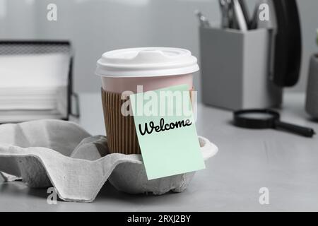 Note autocollante avec le mot Welcome attaché à la tasse de papier de café sur le bureau Banque D'Images