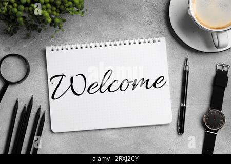 Carnet avec mot Welcome sur la table grise. Bureau avec papeterie et café, plat Banque D'Images