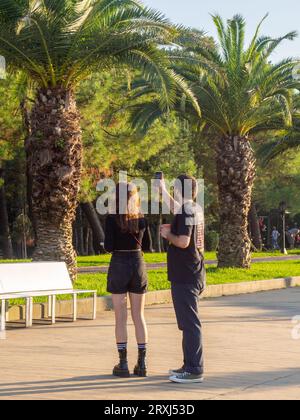 Batumi, Géorgie. 09.15.2023 couple prend des photos dans le parc. Détente parmi les palmiers. Promenez-vous dans le parc de la mer Noire. Gadget en mains Banque D'Images