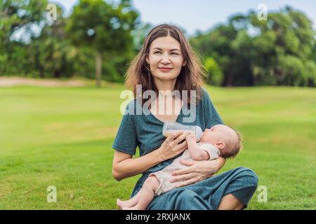 Mère tenant et nourrissant le bébé du biberon dans le parc. Portrait de bébé nouveau-né mignon étant nourri par sa mère en utilisant le biberon. Femme aimante donnant Banque D'Images