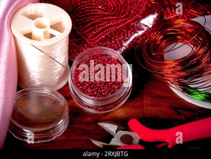 Fabrication de bijoux faits à la main. Boîte avec des perles rouges sur un vieux fond en bois. Accessoires faits main. Vue d'en haut Banque D'Images