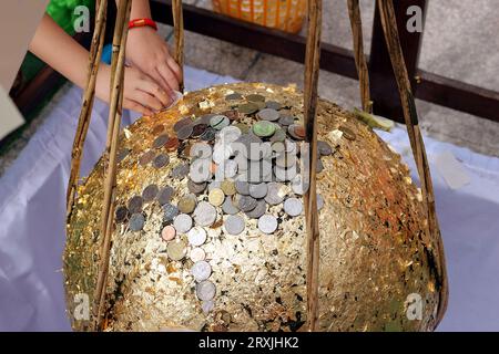 Une photo d'un stupa doré par de jeunes enfants et des personnes âgées, avec le stupa recouvert de feuilles d'or et de nombreuses pièces d'argent placées dessus. Banque D'Images