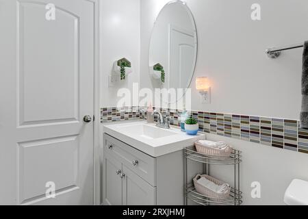 Intérieur de salle de bains minimaliste blanc avec carreaux contrastants multicolores et petit lavabo avec miroir ovale Banque D'Images