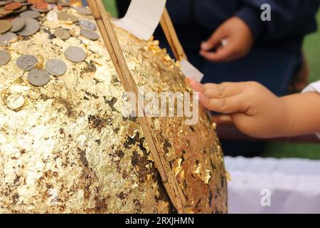 Une photo d'un stupa doré par de jeunes enfants et des personnes âgées, avec le stupa recouvert de feuilles d'or et de nombreuses pièces d'argent placées dessus. Banque D'Images