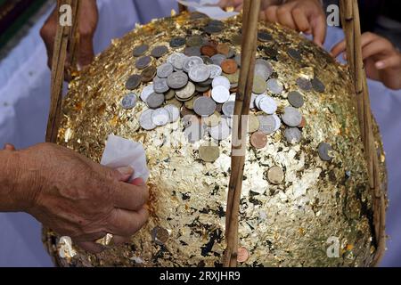 Une photo d'un stupa doré par de jeunes enfants et des personnes âgées, avec le stupa recouvert de feuilles d'or et de nombreuses pièces d'argent placées dessus. Banque D'Images