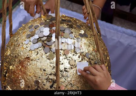 Une photo d'un stupa doré par de jeunes enfants et des personnes âgées, avec le stupa recouvert de feuilles d'or et de nombreuses pièces d'argent placées dessus. Banque D'Images