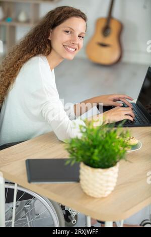 femme d'affaires heureuse confiante en fauteuil roulant à l'aide d'un ordinateur portable Banque D'Images