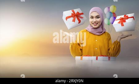 Femme asiatique dans un voile présente une boîte cadeau tout en célébrant une fête d'anniversaire. Concept de femme Joyeux anniversaire Banque D'Images