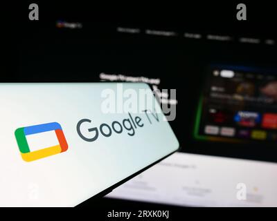 Smartphone avec logo de service de vidéo à la demande Google TV sur l'écran en face du site Web de l'entreprise. Effectuez le focus sur la gauche de l'écran du téléphone. Banque D'Images