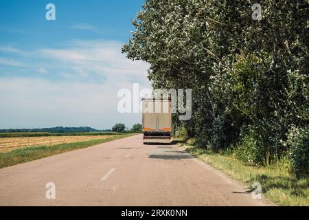 Camionnage et transport de marchandises, vue arrière du grand semi-camion conduisant le long de la route à travers le paysage de campagne en été, diminuant le taux de croissance Banque D'Images