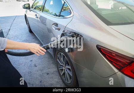 Gros plan d'une femme pompant de l'essence en voiture dans une station-service. Buse de pompe à essence dans le réservoir de carburant d'une voiture grise. Banque D'Images