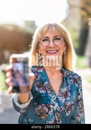 Portrait de femme âgée souriante avec téléphone portable dans la rue Banque D'Images
