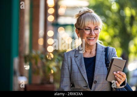 Portrait de femme âgée souriante avec téléphone portable dans la rue Banque D'Images