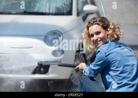 femme utilisant la laveuse électrique pour nettoyer sa voiture Banque D'Images