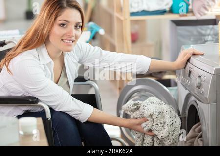 heureuse femme handicapée mettant des chiffons dans une machine à laver Banque D'Images