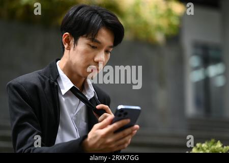 Employé masculin licencié avec boîte de biens à l'aide de smartphone sur les escaliers de l'immeuble de bureaux, perte de travail pendant la récession Banque D'Images