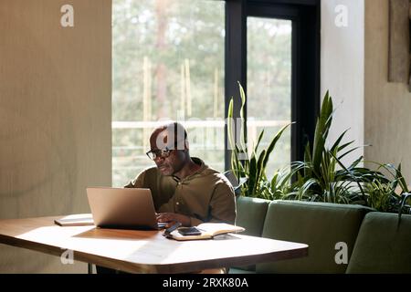 Homme senior afro-américain travaillant sur ordinateur portable assis à table dans un café Banque D'Images
