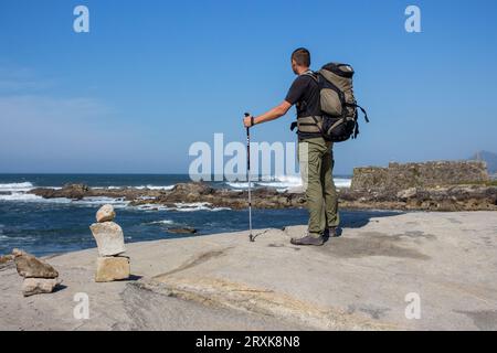 Touriste avec grand sac à dos et bâtons sur la côte de l'océan Atlantique. Pèlerin sur Camino de Santiago, Portugal. Fond de paysage marin pittoresque. Banque D'Images