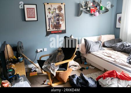 Chambre en désordre de l'adolescent adolescent garçon et vêtements de lit défaits Gorillaz poster chaise gris bleu murs peinture murale peinte Grande-Bretagne UK 2023 KATHY DEWITT Banque D'Images