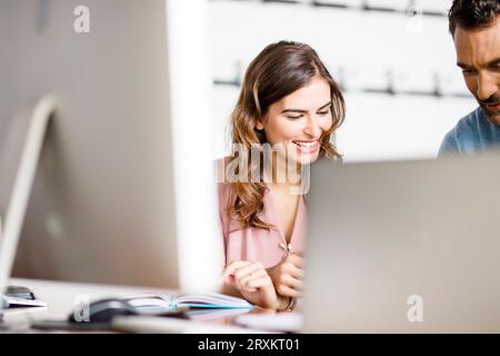 Smiling young businesswoman listening to colleague at desk in office Banque D'Images