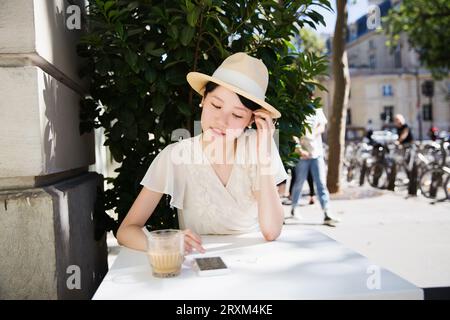 Femme portant un chapeau de paille à l'aide d'un téléphone intelligent à la table Banque D'Images