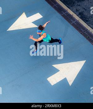 Young woman running sur route avec la flèche signalisation Banque D'Images