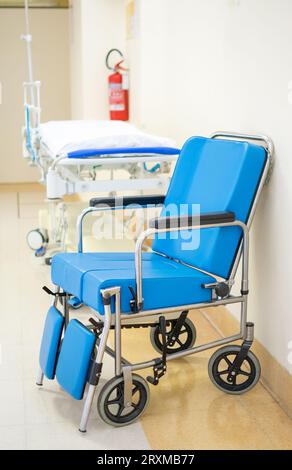 Fauteuil roulant rembourré bleu spécialisé avec civière d'hôpital dans le fond de couloir Banque D'Images