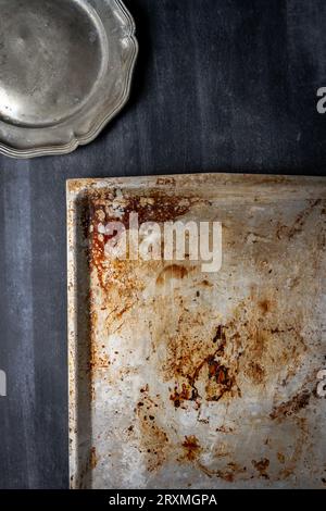 Moule plat de four usagé avec des taches brûlées et des rayures et plaque d'étain sur fond noir de tableau noir Banque D'Images