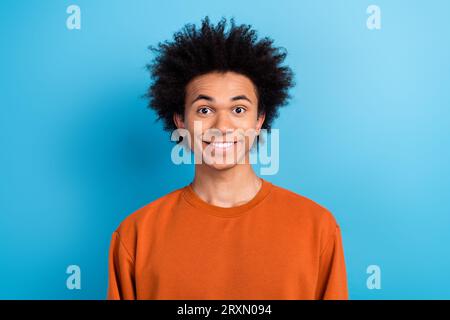 Portrait de candide sincère optimiste gars avec coiffure afro habillé pull brun toothy souriant isolé sur fond de couleur bleue Banque D'Images