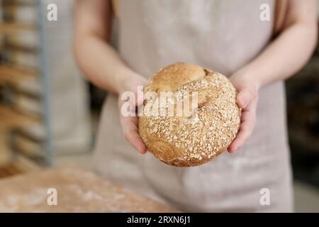 Gros plan de la jeune femme tenant un pain de blé entier frais décoré avec des graines dans la boulangerie, espace de copie Banque D'Images