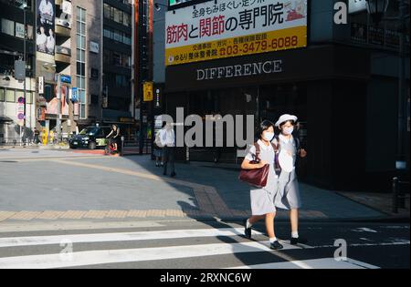 Deux écolières japonaises ensoleillées traversent la raod à Roppongi, Tokyo, Japon Banque D'Images