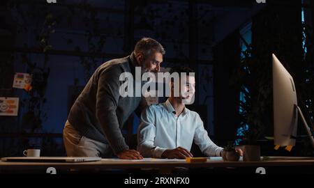 Portrait de deux collègues masculins travaillant sur un projet commun longtemps dans la nuit au bureau Banque D'Images
